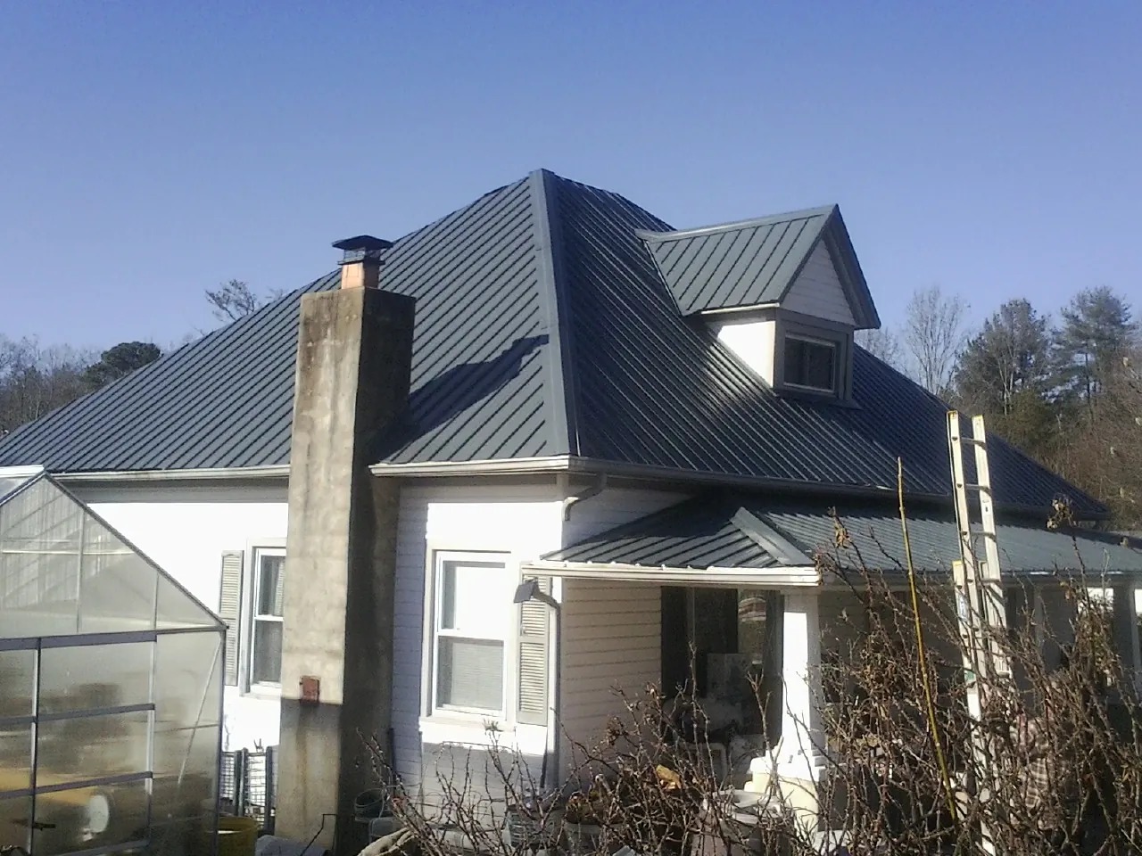 Dark blue standing seam metal roof on a white farmhouse with dormer — Slate & Tile Roof Repair by Roofing Brothers in Polk City