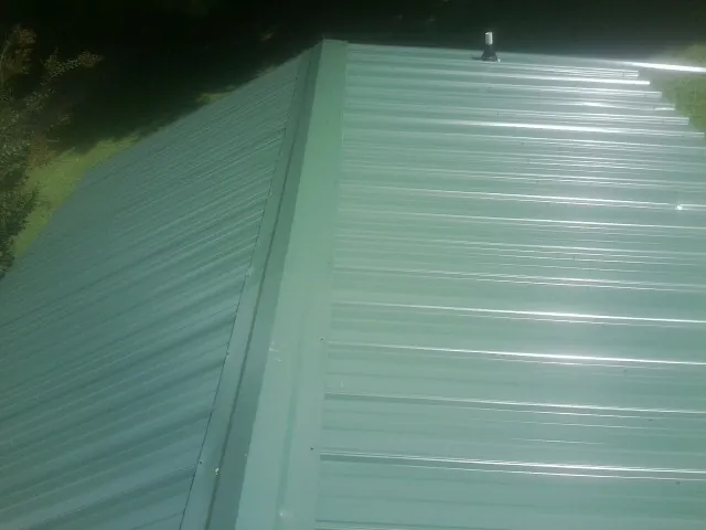 New green metal panels meeting at the ridge of a roof — Flat Roof Repair work by our crew in Polk City