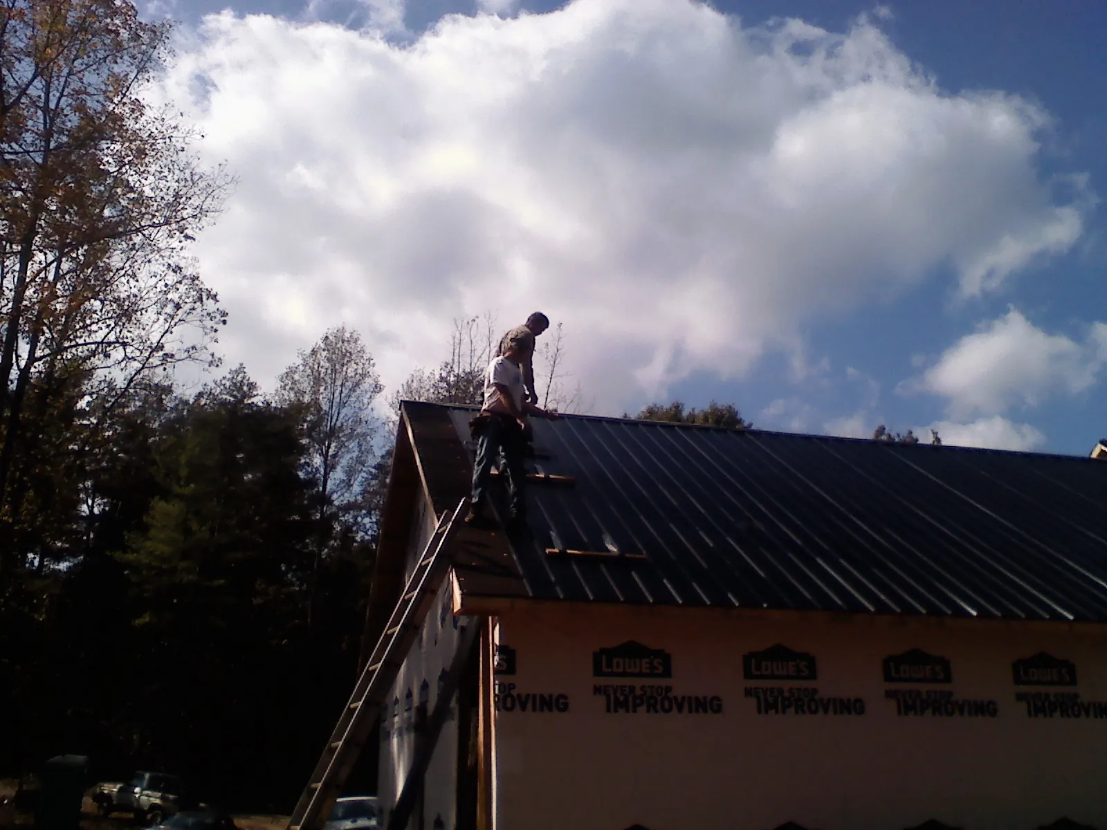 Roofer fastening dark metal panels high against a cloudy sky, from a Roof Inspection job in Polk City